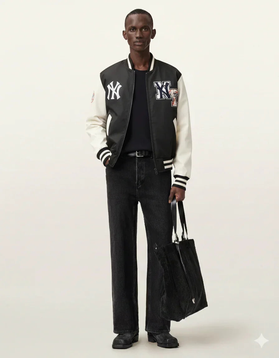 Man wearing black and white varsity jacket with NY logo, black jeans, holding tote bag