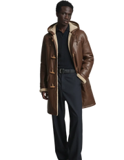 Men's brown shearling coat with hood and toggle closures, styled with dark pants and sweater